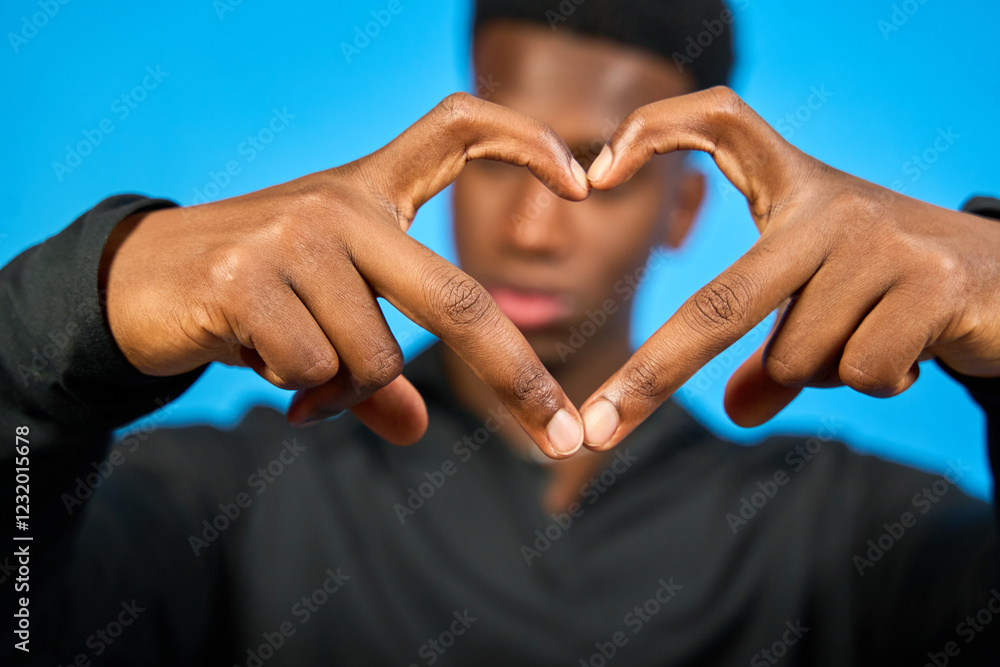 Young man making heart shape with hands on blue background Young man making heart shape with hands on blue background