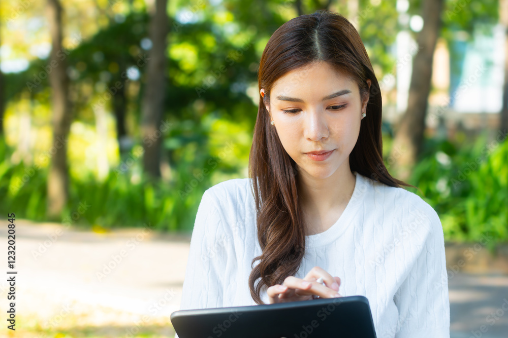 Young Asian female student using digital tablet sits in a sunny park. Asian woman remote education, online learning, and researching information for her virtual course while sits in a tranquil park. Young Asian female student using digital tablet sits in a sunny park. Asian woman remote education, online learning, and researching information for her virtual course while sits in a tranquil park.