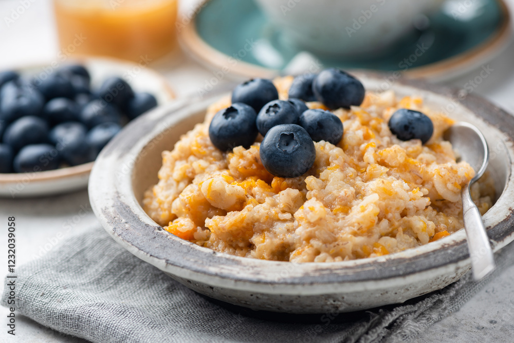 Oatmeal porridge with pumpkin topped with fresh blueberries. Hearty warm oatmeal bowl for cozy autumn morning breakfast Oatmeal porridge with pumpkin topped with fresh blueberries. Hearty warm oatmeal bowl for cozy autumn morning breakfast