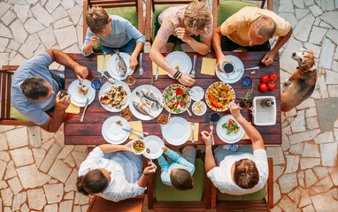 Top view of cheerful family gathered around outdoor dining table enjoying Mediterranean meal with fresh fish, vegetables, and salads, vibrant dishes on rustic terrace, summer vibe, togetherness.