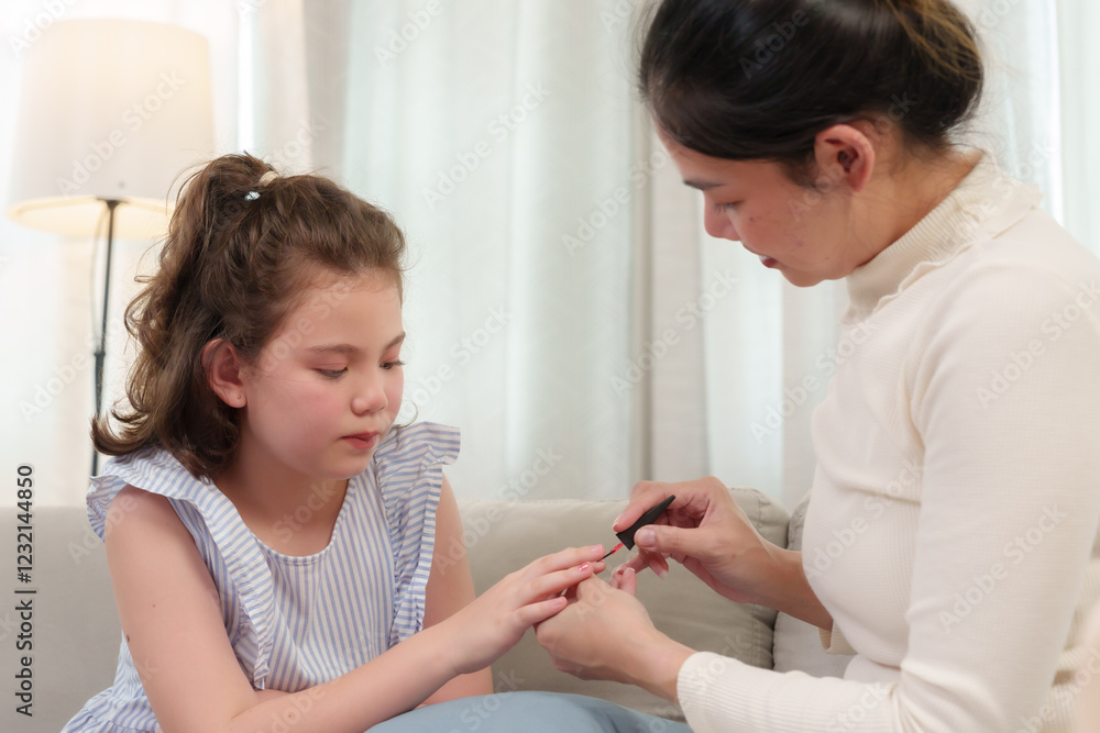 Happiness of Caucasian daughter and Asian mother. Mother carefully painting daughter’s nails. Girl observing with a calm expression. Sweet and relaxing beauty bonding moment at home. Happiness of Caucasian daughter and Asian mother. Mother carefully painting daughter’s nails. Girl observing with a calm expression. Sweet and relaxing beauty bonding moment at home.