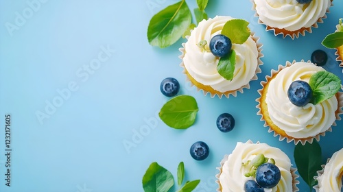 Beautiful lemon vanilla cupcakes with cream cheese frosting decorated with fresh blueberries and green leaves. Delicious homemade dessert. Festive bakery. Blue background. Copy space. Close up food.