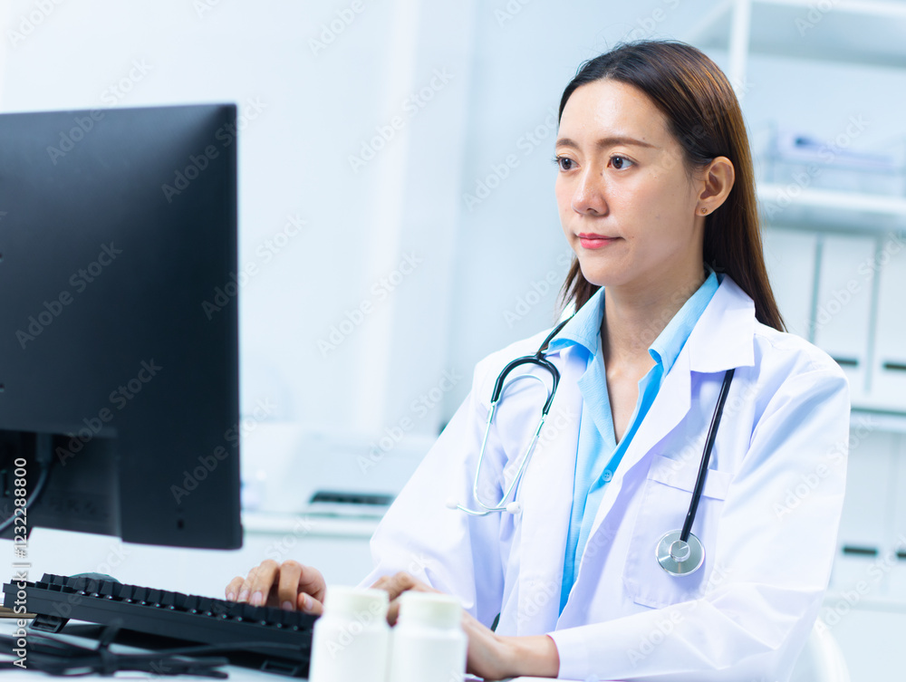 Focused young Asian Professional female doctor in uniform with a stethoscope working on a computer for medical service, online research, and telehealth sits at desk in a doctor room hospital. Focused young Asian Professional female doctor in uniform with a stethoscope working on a computer for medical service, online research, and telehealth sits at desk in a doctor room hospital.