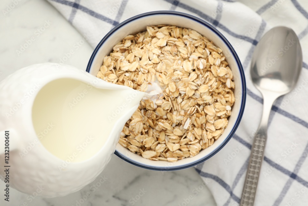 Pouring milk into bowl with oatmeal at white marble table, top view Pouring milk into bowl with oatmeal at white marble table, top view