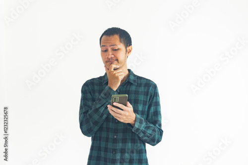 Young man wearing green flannel is thinking while using smartphone on isolated white background photo