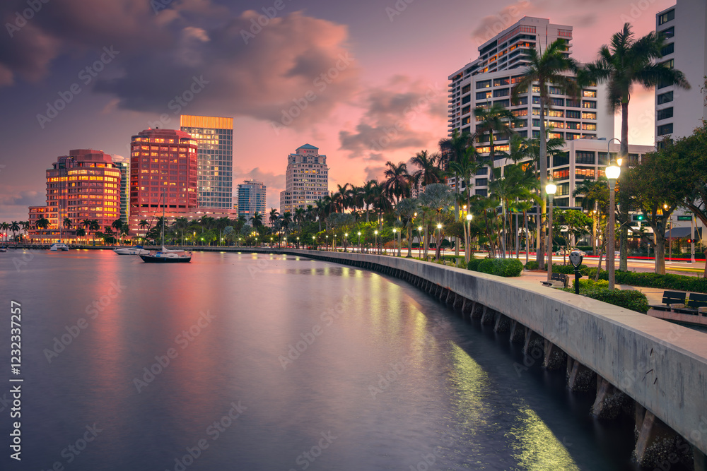 West Palm Beach, Florida, USA. Skyline of West Palm Beach, Florida, at dusk. Tall buildings with reflective glass facades line the waterfront, casting colorful reflections on the water.