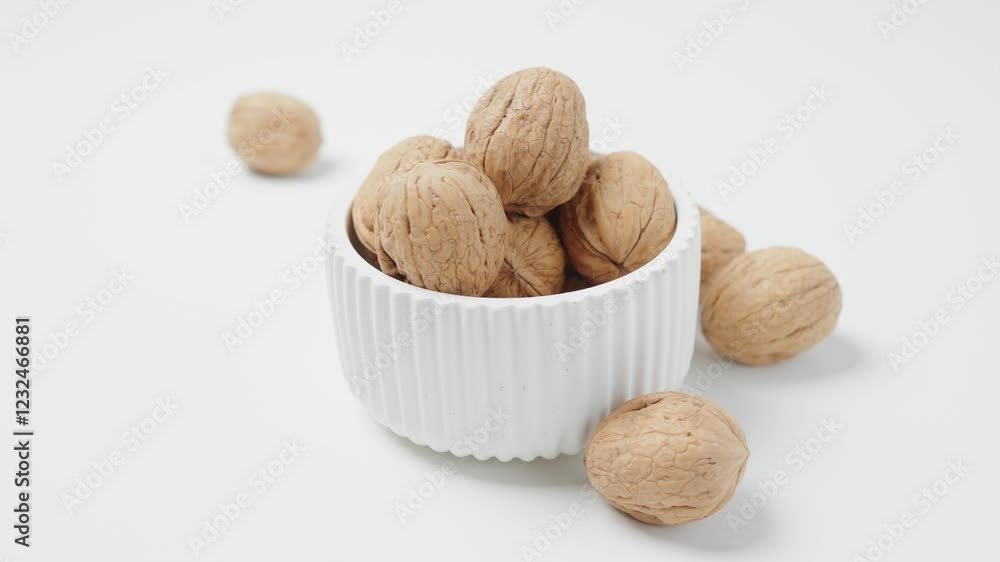 Hand Reaching for Walnuts in White Ceramic Bowl on Light Background Hand Reaching for Walnuts in White Ceramic Bowl on Light Background