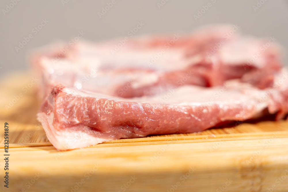 A piece of meat is on a wooden cutting board. The meat is cut into thin slices. The meat is white in color A piece of meat is on a wooden cutting board. The meat is cut into thin slices. The meat is white in color
