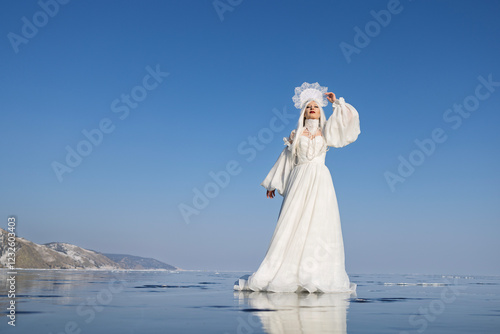 A woman in a white dress and traditional headdress on icy lake. Winter fairy tale, Snow Queen concept.