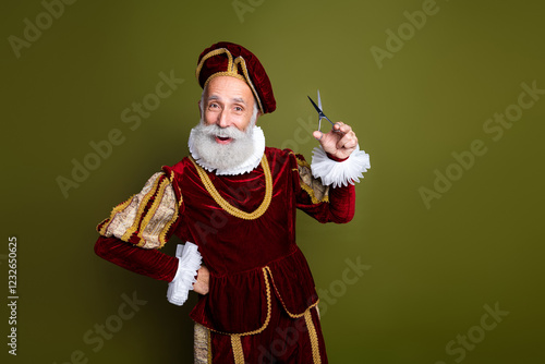 Charming elder man in a historical costume holding scissors on a khaki background photo