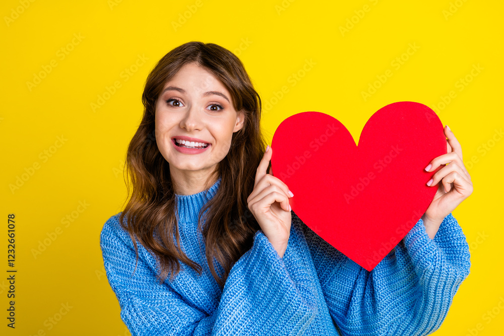 Smiling young woman holding a large red heart figure against a vibrant yellow background Smiling young woman holding a large red heart figure against a vibrant yellow background