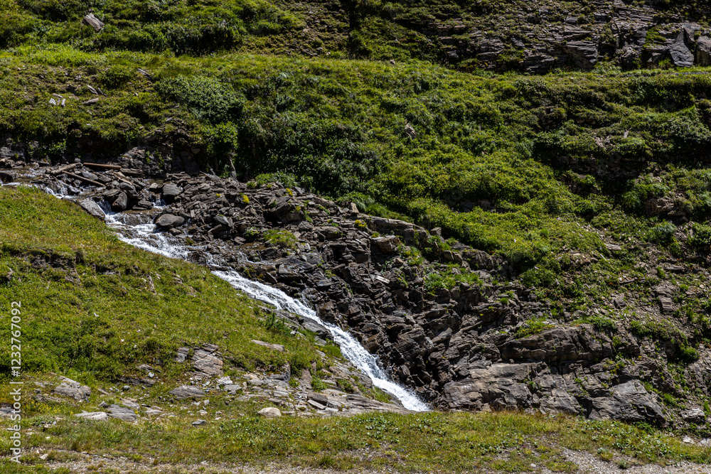 Grossglockner mountain range in Austria with green slopes, stream and rocks in the foreground Grossglockner mountain range in Austria with green slopes, stream and rocks in the foreground