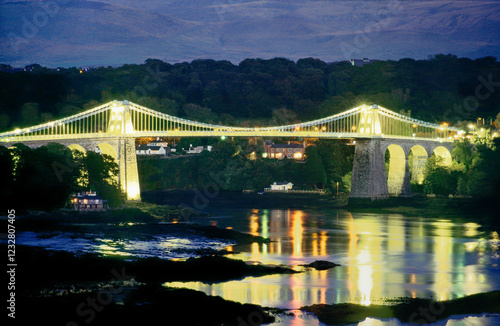 The Menai Suspension Bridge built by Thomas Telford 1826 crosses the Menai Strait to Anglesey, Gwynedd, north Wales. Floodlit photo