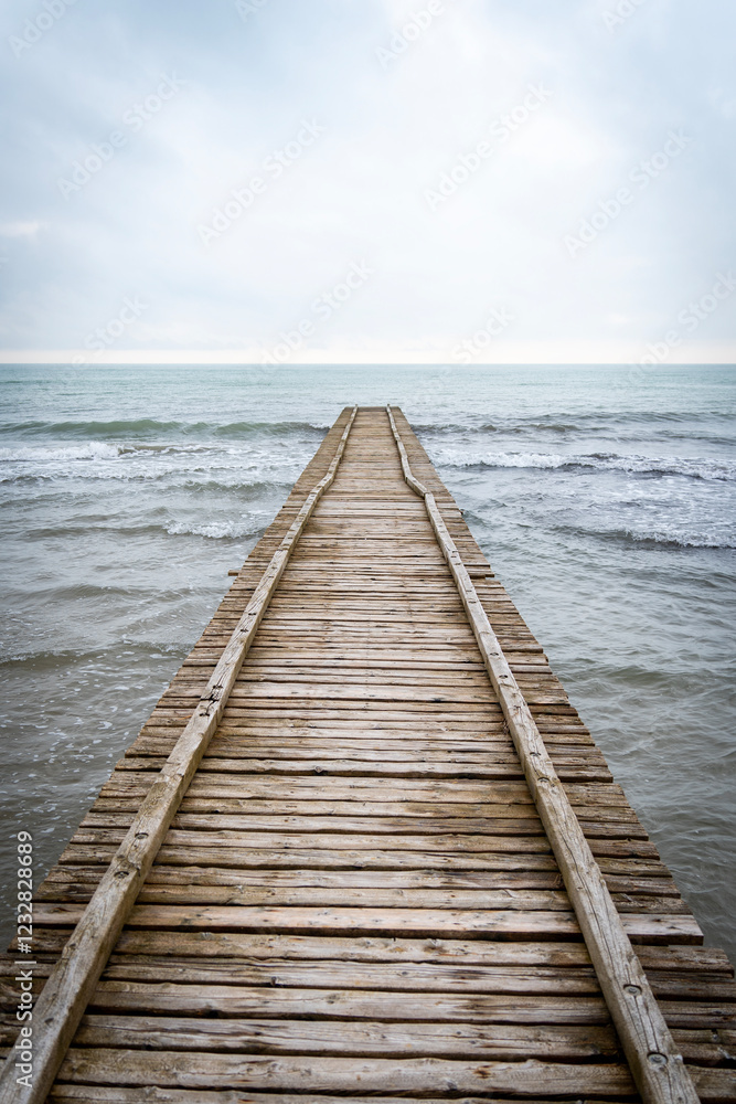 Obraz premium Wooden pier leading to the Adriatic Sea on a cloudy autumn beach in Italy