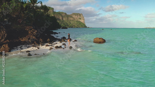 Woman enjoying a moment of peace while walking on a white sand beach with turquoise water and lush vegetation in the background