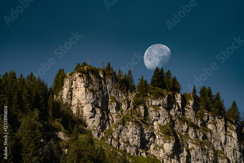 Full moon in daylight behind a mountain