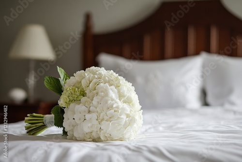 Elegant white hydrangea bouquet resting on a bed in a cozy hotel room before ...
