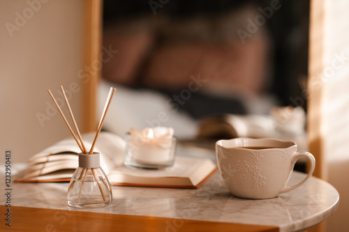 Obraz na plátně Cup of coffee with aroma diffuser and burning candle on paper book staying on marble table in room close up