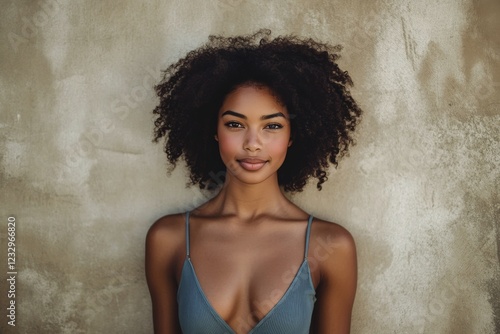 Portrait of a young woman with curly hair against a rustic wall showcasing na...