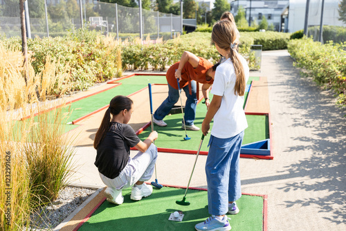 Cute school girl playing mini golf with family. Happy toddler child having fun with outdoor activity. Summer sport for children and adults, outdoors. Family vacations or resort. photo