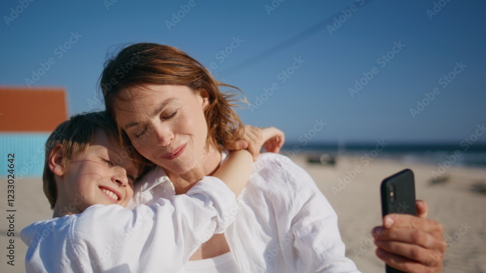 Woman son taking picture on smartphone hugging on sandy beach kissing closeup. Woman son taking picture on smartphone hugging on sandy beach kissing closeup.