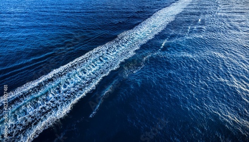 aerial view of ocean water wake pattern left by a boat showing turbulent waves and trail on deep blue sea surface