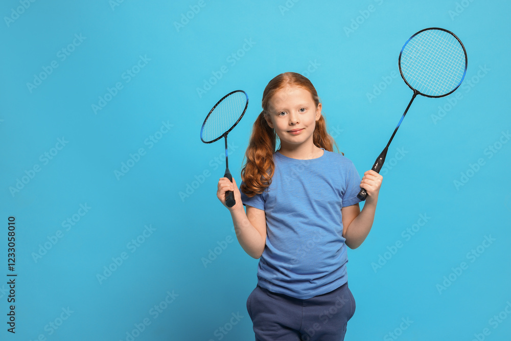 Little girl with badminton rackets on light blue background, space for text Little girl with badminton rackets on light blue background, space for text