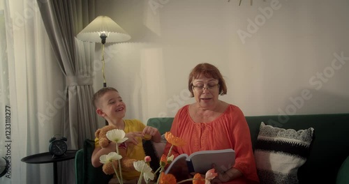 Grandma and her little grandson reading a book, child with grandma, smiling, expressing happiness, grandchild with loving grandma at home, enjoying reading fairy tales together.