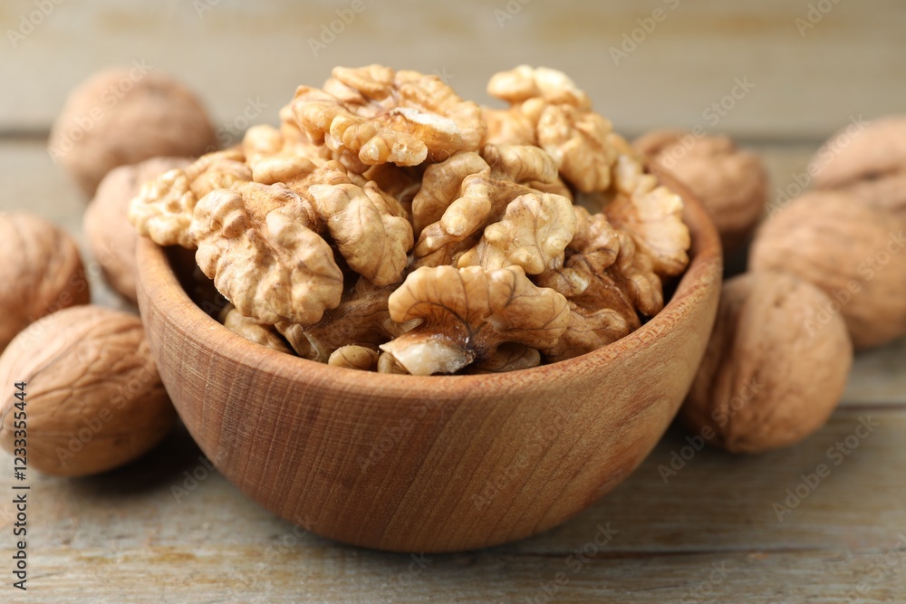 Peeled walnuts in bowl and whole ones on wooden table, closeup Peeled walnuts in bowl and whole ones on wooden table, closeup