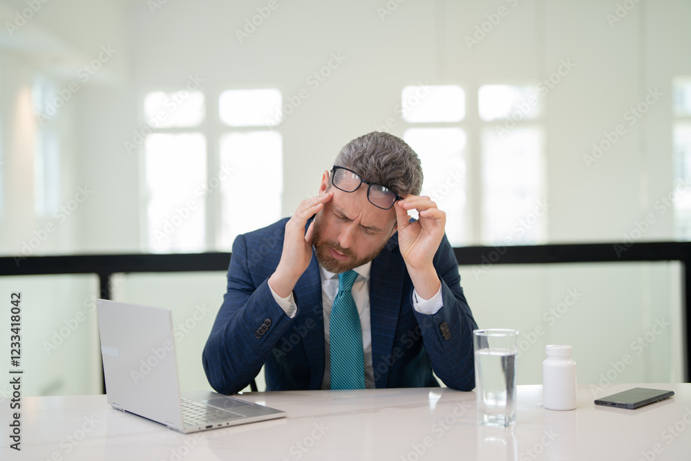 Stressed business man having headache at office. Tired businessman is working overtime and has headache. Overworked man with laptop at workplace, suffers from headache. Migraine from overwork. Stressed business man having headache at office. Tired businessman is working overtime and has headache. Overworked man with laptop at workplace, suffers from headache. Migraine from overwork.