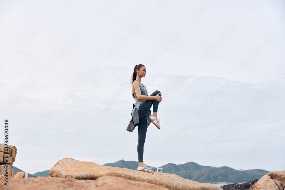 Fit young woman practicing yoga on rocky terrain in athletic wear, showcasing strength and balance against a serene natural backdrop Fit young woman practicing yoga on rocky terrain in athletic wear, showcasing strength and balance against a serene natural backdrop