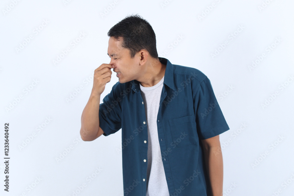 Asian man holds his nose with his hand because he has a cold and has a dust allergy Asian man holds his nose with his hand because he has a cold and has a dust allergy