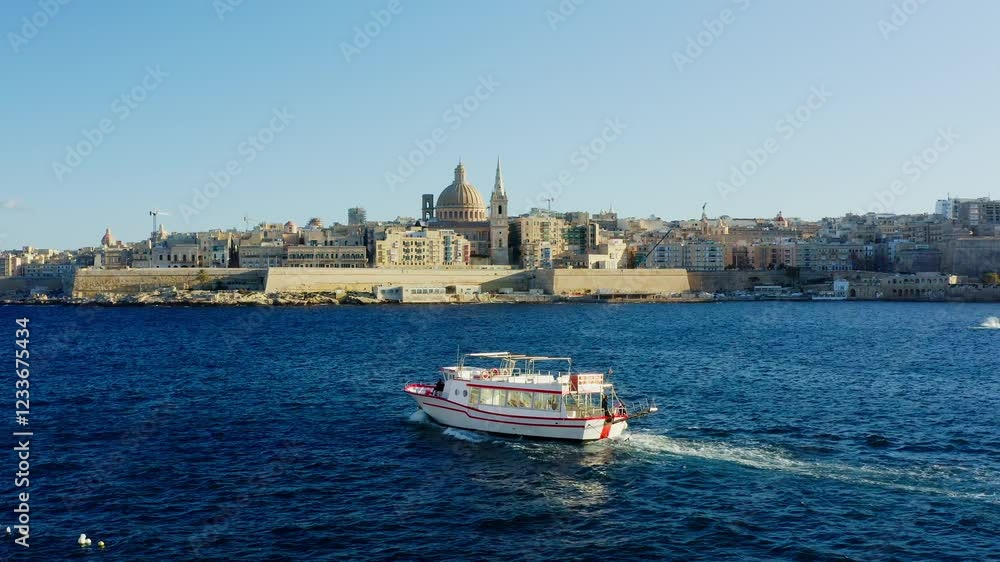 Aerial scenic shot of a tourist boat sailing with Valletta and St Paul Cathedral in the background, Malta drone. Aerial scenic shot of a tourist boat sailing with Valletta and St Paul Cathedral in the background, Malta drone.