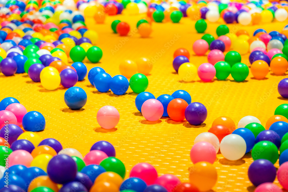 Obraz premium A vibrant scene of colorful plastic balls scattered across a bright yellow play surface.