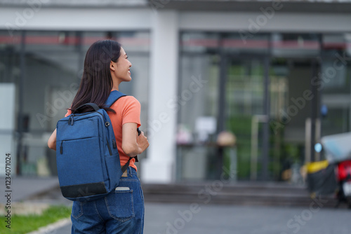 Happy university student wearing backpack walking outside campus building, enjoying fresh air and looking away, feeling excited about new semester photo