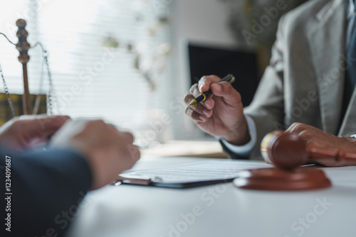 Lawyer holding a pen while explaining contract details to a client in a law firm or notary office, with a gavel and scales of justice prominently displayed on the desk