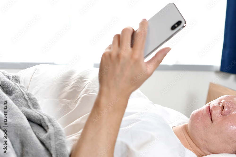 ベッドで寝ながら笑顔でスマホを使う男性 ベッドで寝ながら笑顔でスマホを使う男性