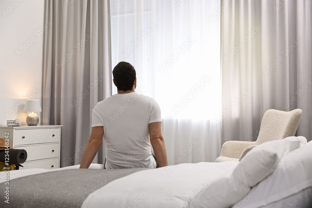 Traveller sitting on bed in hotel room, back view Traveller sitting on bed in hotel room, back view