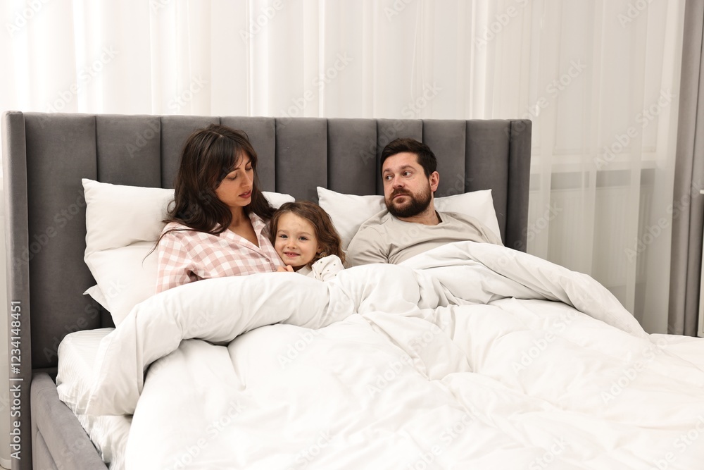 Fototapeta premium Happy playful daughter with her overwhelmed parents in bed at home