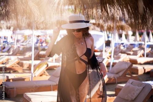 Foto A fashionable woman in a black swimsuit and sheer cover-up enjoys a sunny day at a luxurious beach resort with straw umbrellas