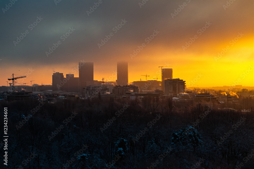 Winter sunrise landscape in Bucharest, highlighting the sun surrounded by glowing clouds and silhouetted buildings. Construction industry in Romania. Residential area in the North of Bucharest