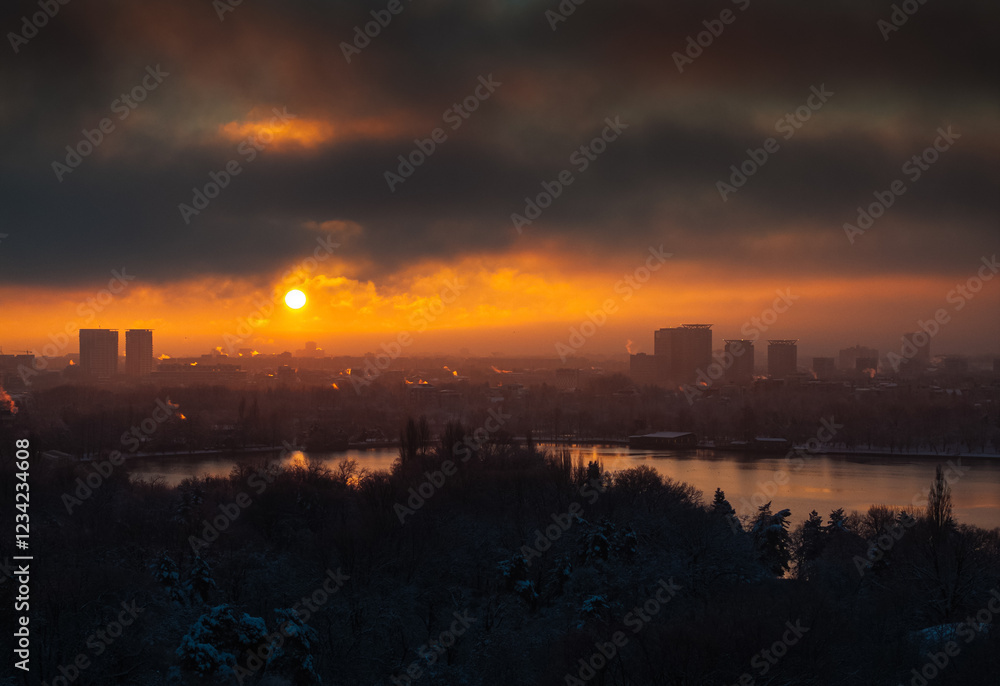 Bucharest from above. A vibrant winter sunrise in Bucharest, featuring an orange-hued sky with the sun casting light on the city skyline and surrounding nature, creating a dynamic contrast.