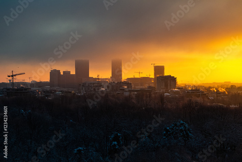 Obraz na płótnie Winter sunrise landscape in Bucharest, highlighting the sun surrounded by glowing clouds and silhouetted buildings. Construction industry in Romania. Residential area in the North of Bucharest w salonie