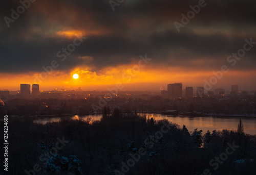 Obraz na płótnie Bucharest from above. A vibrant winter sunrise in Bucharest, featuring an orange-hued sky with the sun casting light on the city skyline and surrounding nature, creating a dynamic contrast. w salonie