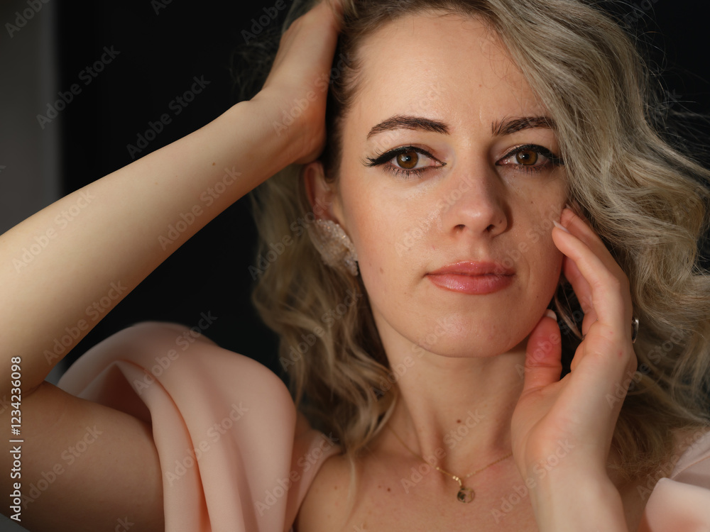 Fototapeta premium A close-up portrait of a stylish woman with wavy blonde hair, elegant silver rings, and soft makeup, gazing confidently at the camera against a dark background