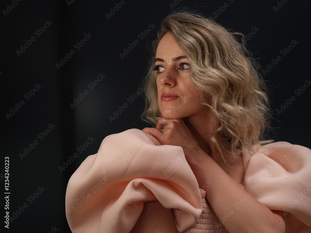 Fototapeta premium A stylish woman in a pink dress with puffed sleeves gazes off-camera with a poised expression, exuding confidence and sophistication against a dark background