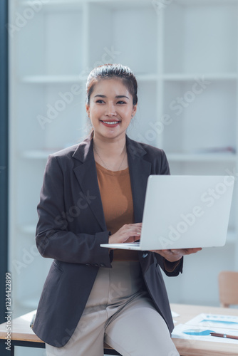 Billede på lærred Confident Businesswoman with Laptop: A smiling, young businesswoman exudes confidence as she works on her laptop, showcasing professionalism and success in a modern office setting