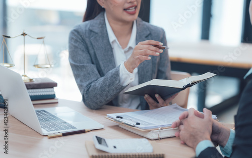 Legal Consultation: A female lawyer confidently explains legal matters to a client, using documents and a laptop in a professional office setting. The image conveys trust and expertise. 