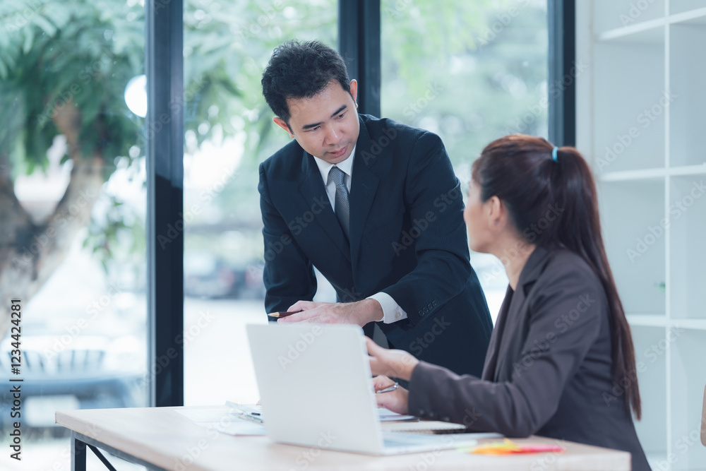Business Colleagues Collaboration: A focused business meeting unfolds as a male and female colleague collaborate intently over a laptop.