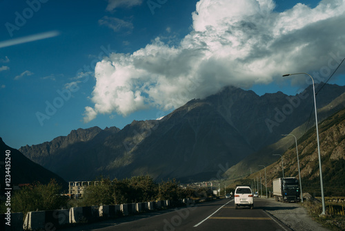 A white car is driving on a mountain road. The ridges of the North Caucasus are on the background. Stunning mountain road in Georgia photo